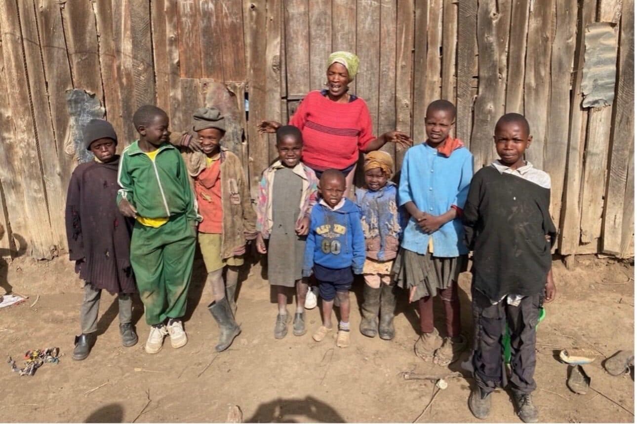 A woman standing with eight children in front of their home in Kenya